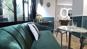 A green sofa with a white pillow, a small round table with a vase, and a wall-mounted mirror. - La Belle Endormie B&B (Bordeaux)