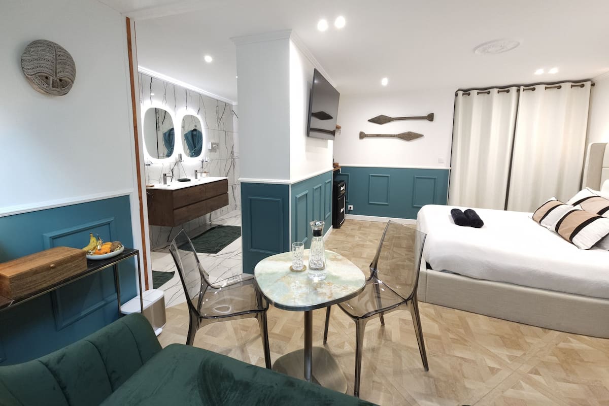 Une chambre d’hôtel moderne équipée d’un lit, d’un canapé, d’une table à manger et d’un coin cuisine avec un évier et des miroirs.