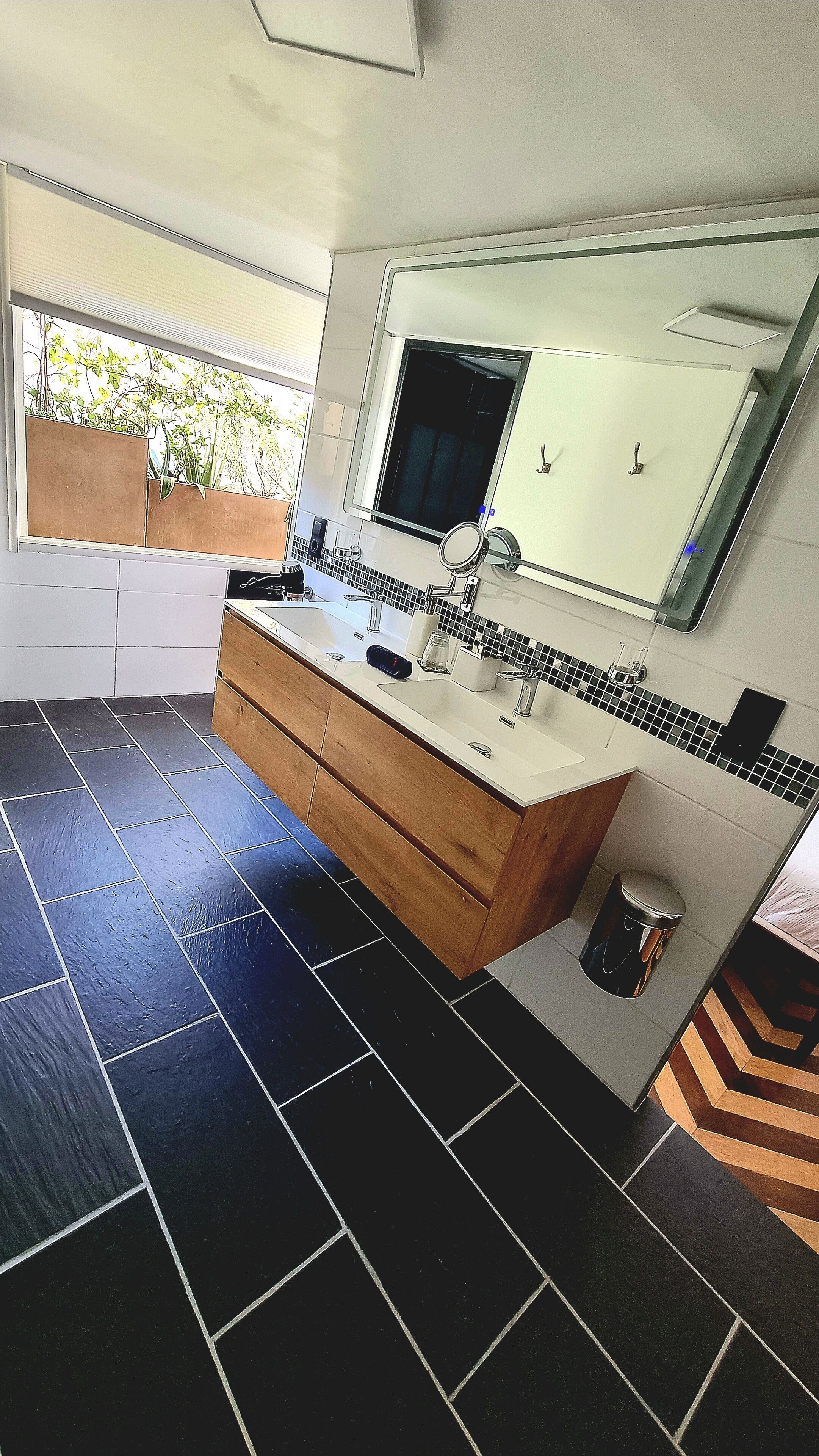 Un baño moderno con lavamanos doble, un espejo grande y una ventana con plantas.