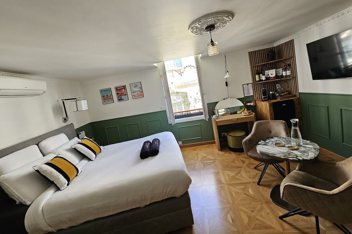 Une chambre d’hôtel avec un lit, un bureau, une chaise, une télévision et une étagère avec des bouteilles.