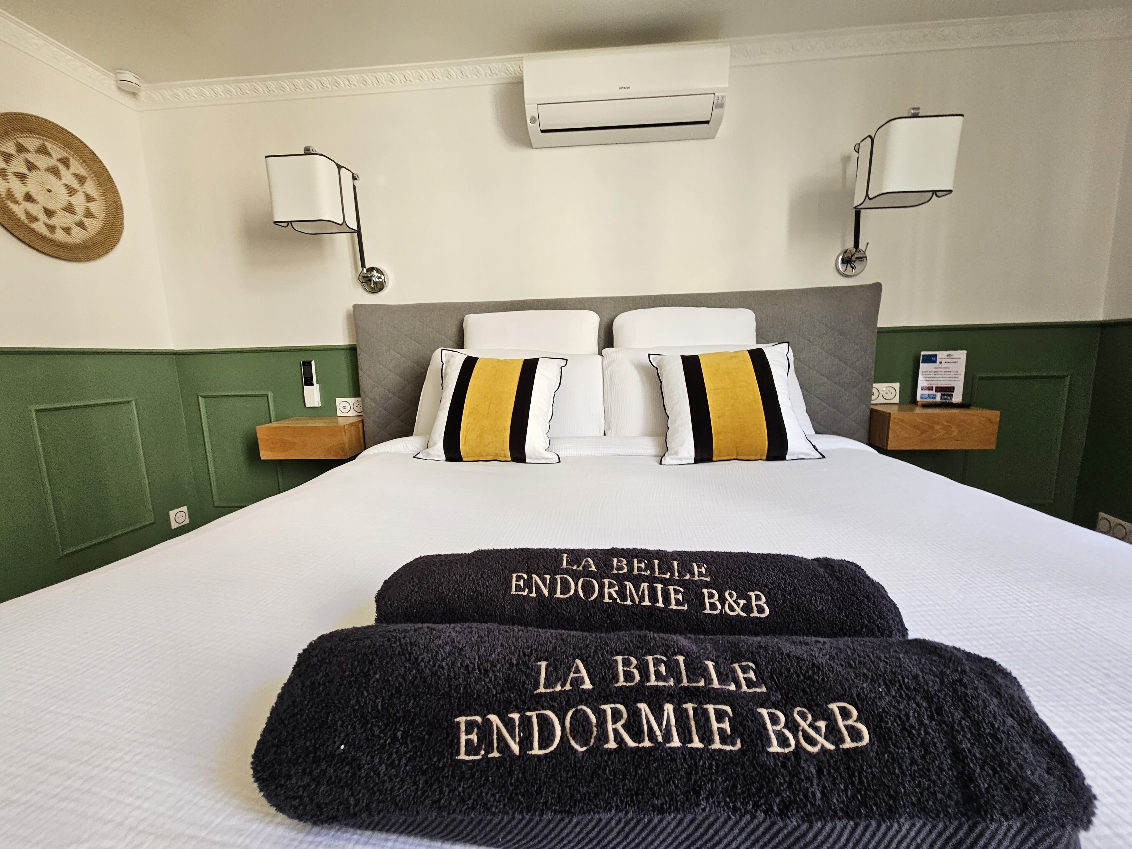 Una habitación de hotel con una cama grande, dos mesitas de noche, aire acondicionado en la pared y una lámpara mural.