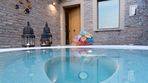 A swimming pool with a brick wall backdrop, two lanterns, and a stack of colorful towels. - Splendid Villa Monte Quercione (Emilia-Romagna)