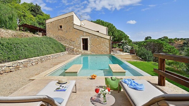 Um edifício de pedra com piscina, área de estar ao ar livre e vista para a paisagem circundante.