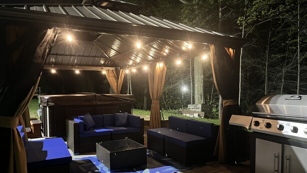 En udendørs patio med grill, siddepladser og lyskæder.