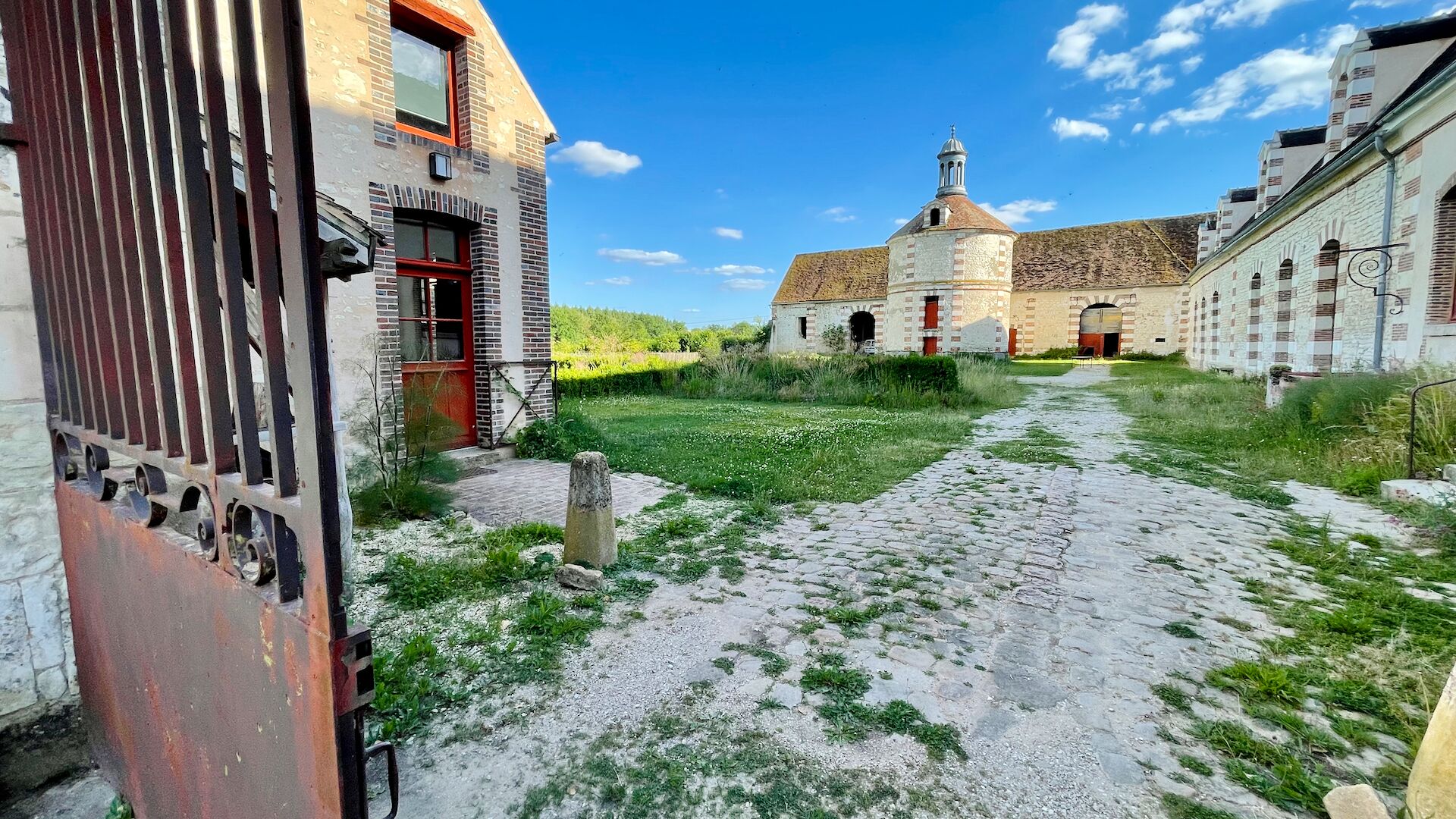 A courtyard with cobblestone paths, a red door, and a building with a bell tower.