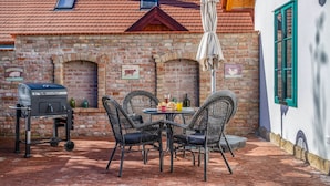Un patio con pared de ladrillo, una parrilla, sillas de mimbre y una mesa con bebidas.