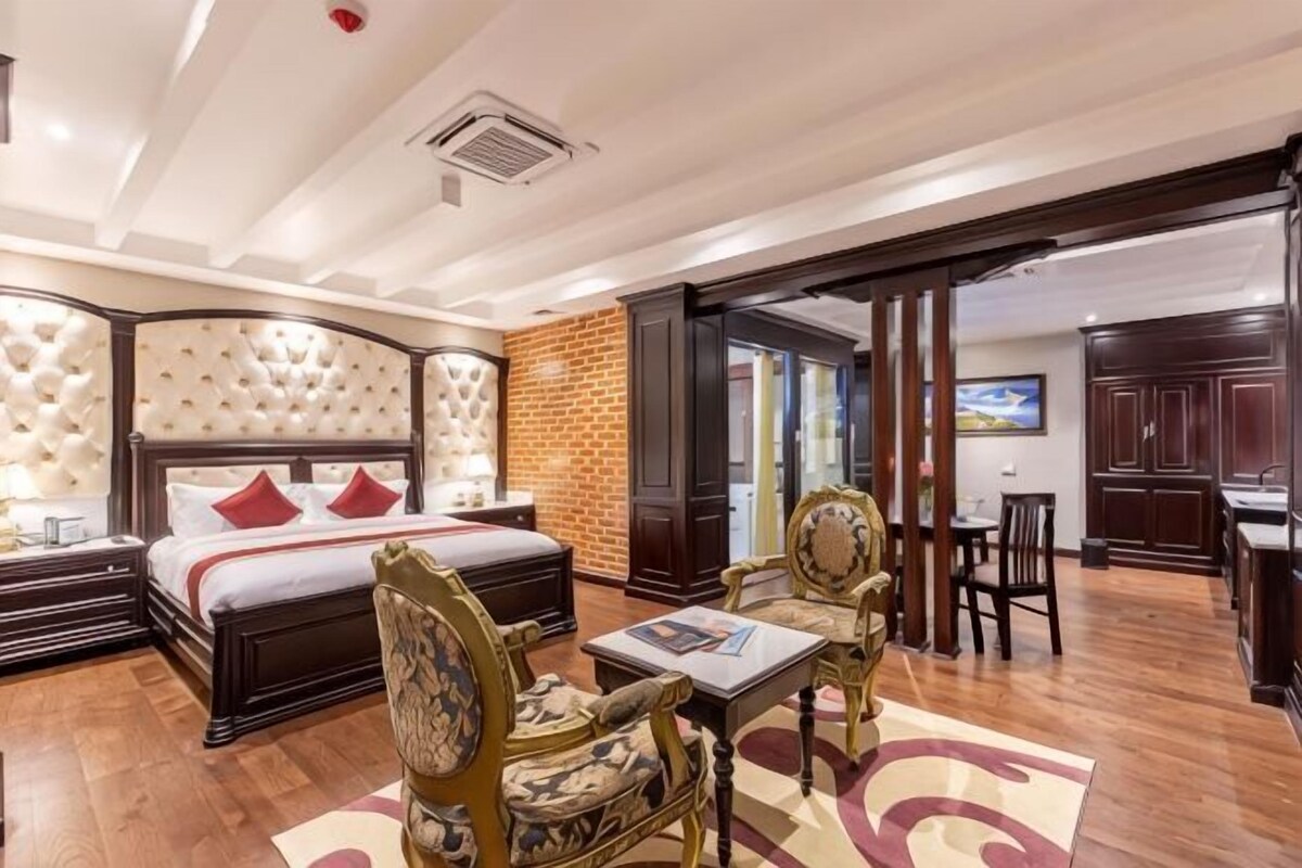 A hotel room with a large bed, a desk, two chairs, a small table, and a brick wall.
