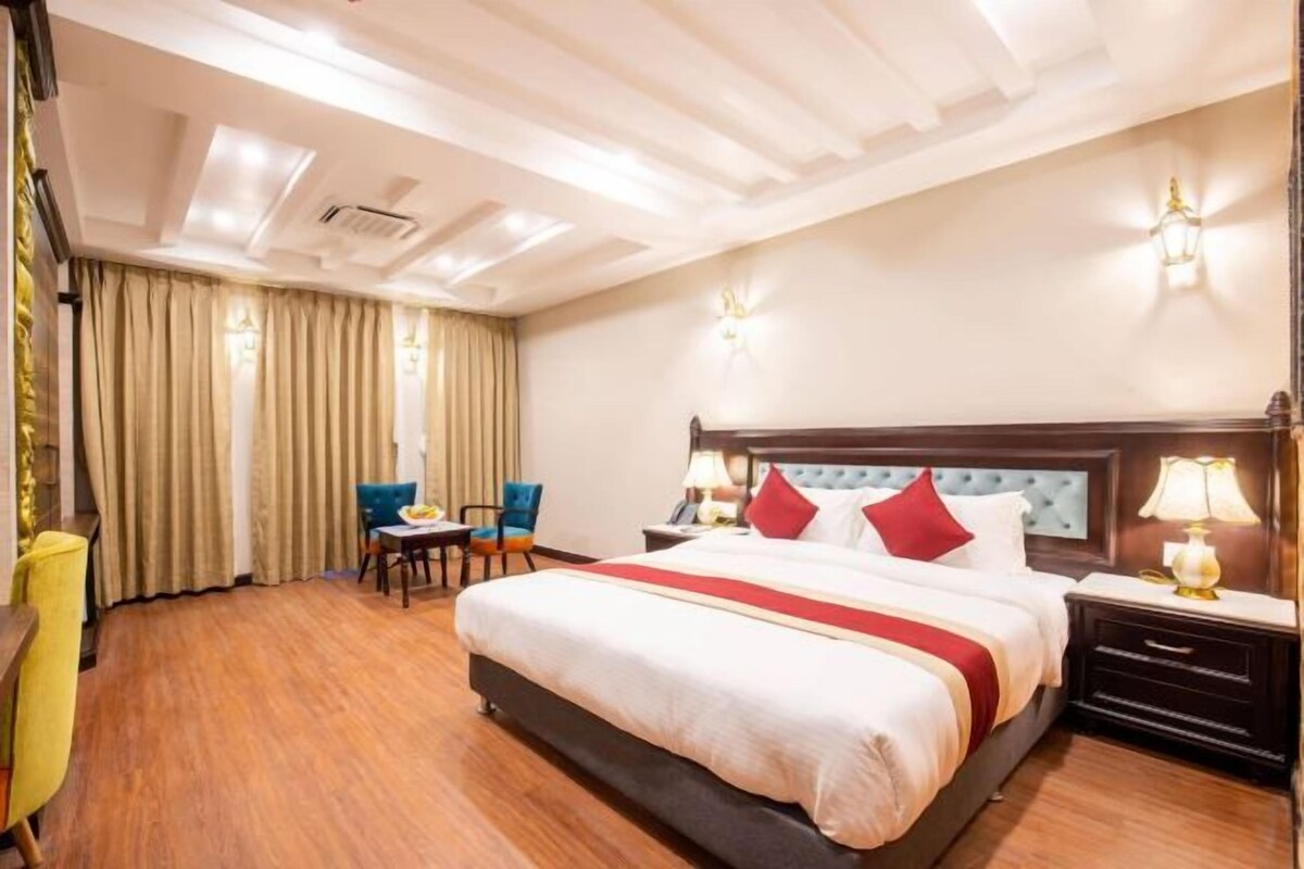 Una habitación de hotel con una cama grande, un escritorio con silla, una lámpara y una ventana con cortinas.