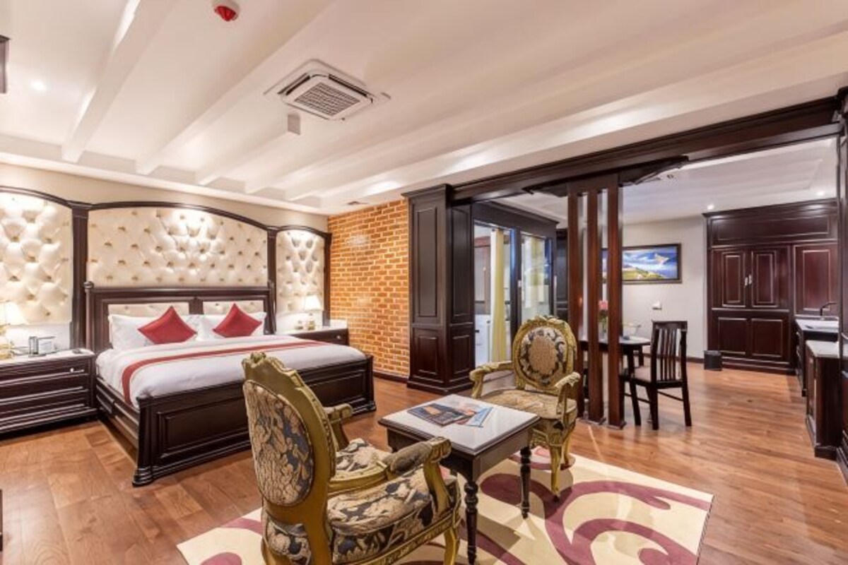 A hotel room with a large bed, a desk, two chairs, a small table, and a brick wall.