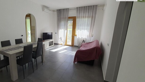 Une chambre moderne avec une table à manger, des chaises, un téléviseur et un lit recouvert d’une couverture rouge.