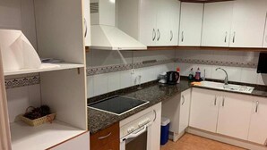 Eine kleine Küche mit weißen Schränken, einem Backofen, einem Spülbecken und einer Arbeitsfläche mit Wasserkocher und Reinigungsmitteln.