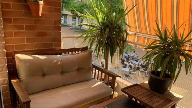 Ein Balkon mit einer beigefarbenen Couch, einem Holztisch und Topfpflanzen.