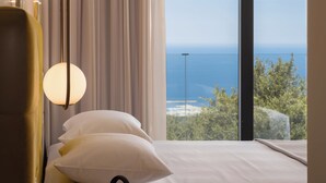 Un lit avec une literie blanche et une vue sur l’océan par une grande fenêtre.