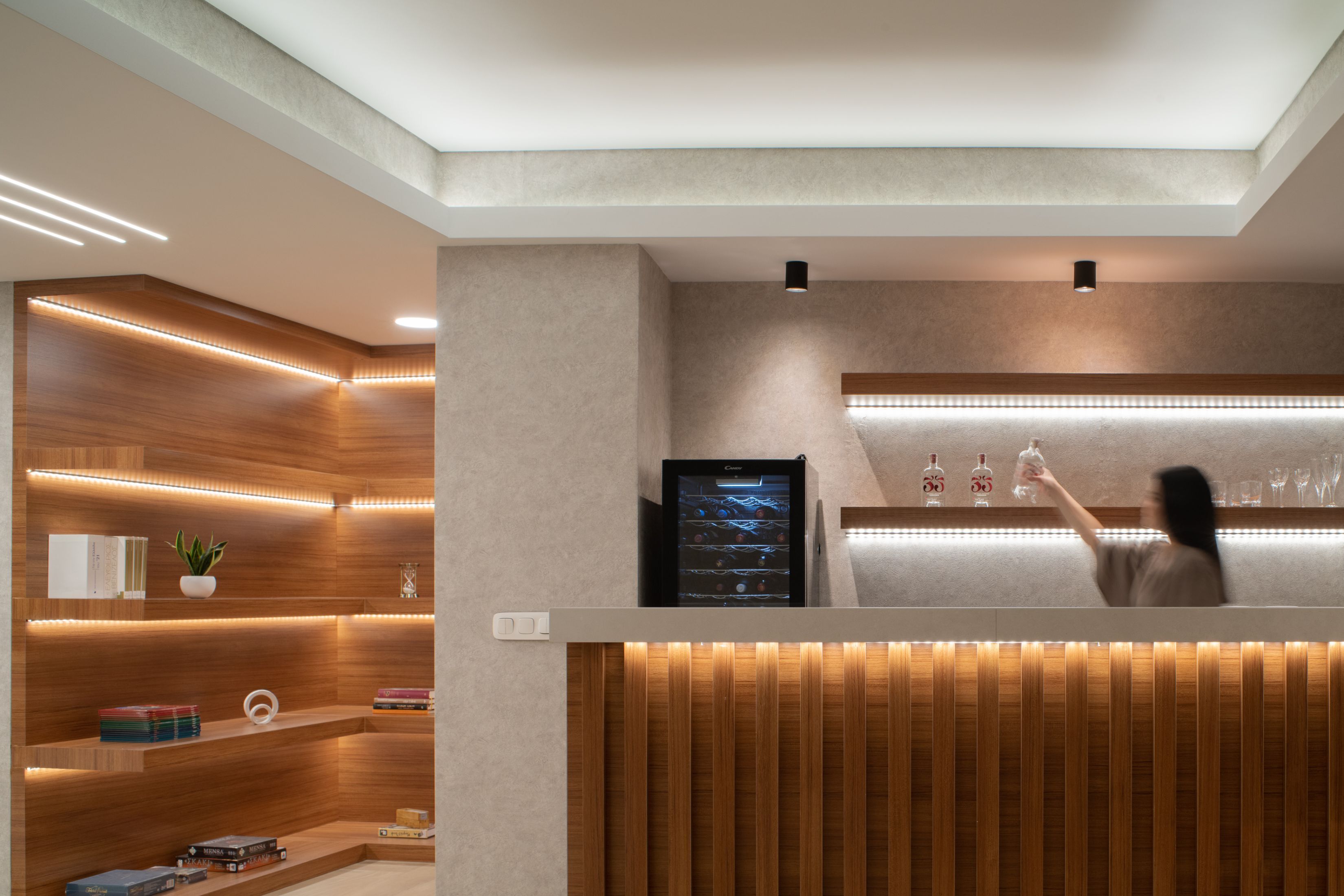 Een moderne bar met houten lambrisering, een digitaal scherm en planken met boeken en glazen.