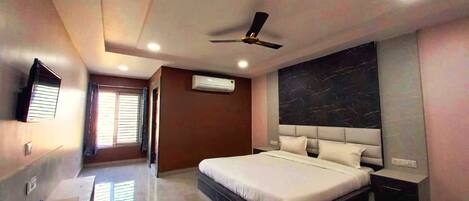A modern bedroom with a large bed, a ceiling fan, an air conditioning unit, a flat-screen TV, and a marble accent wall.