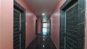 Un pasillo largo y estrecho con paredes rosas y puertas de mármol negro, que da paso a una habitación luminosa al final.