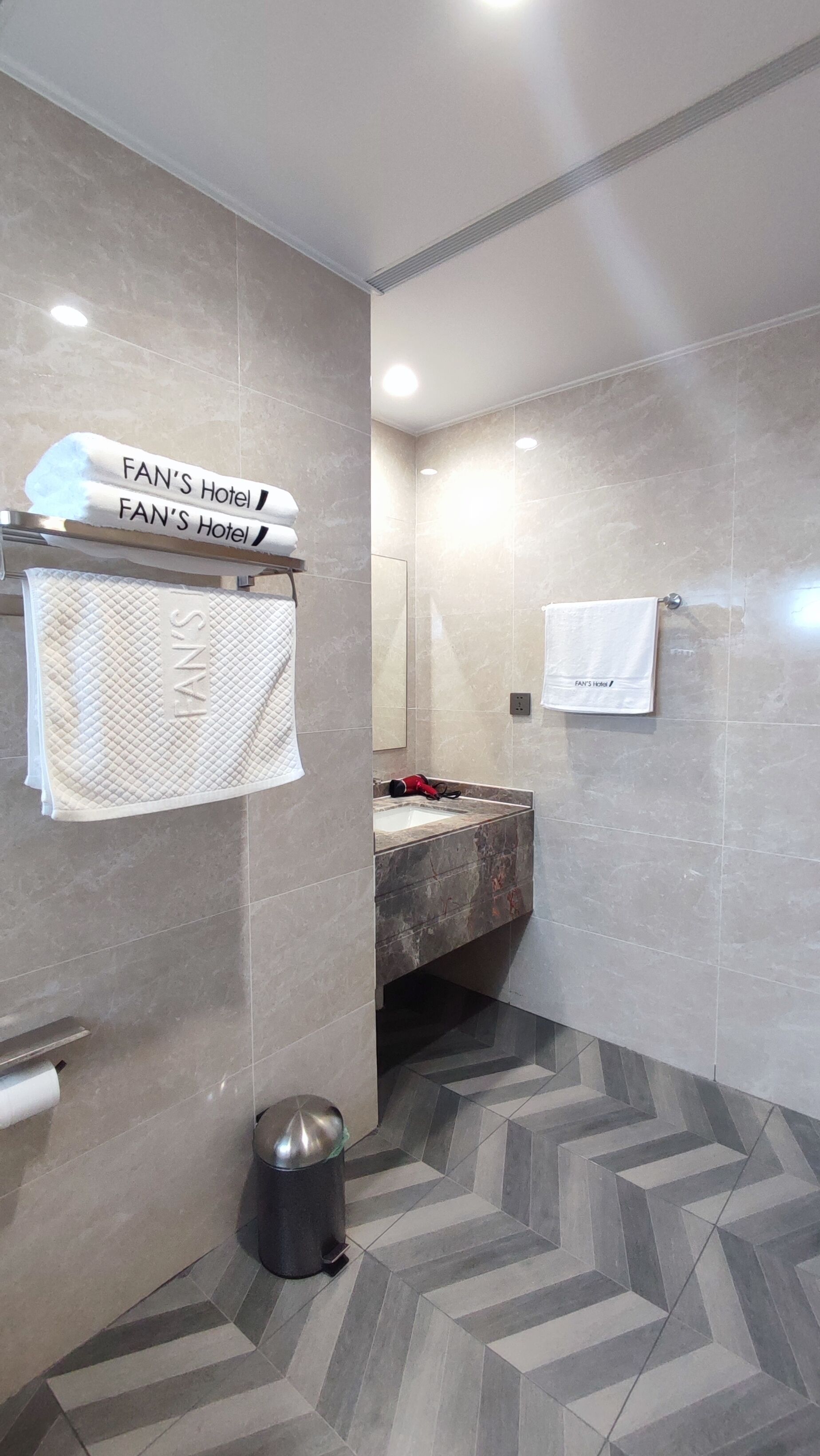 A modern bathroom with a herringbone tile floor, a sink, and a towel rack with towels labeled "FAN'S Hotel".