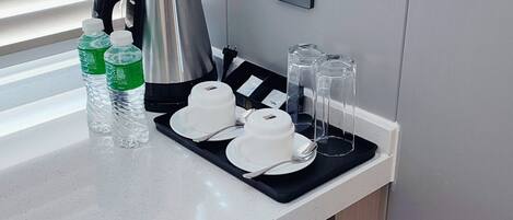 A kitchen counter with a kettle, water bottles, cups, and glasses.