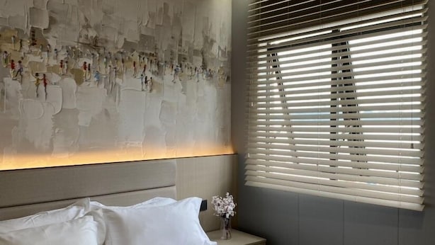 A modern bedroom with a large bed, a headboard with a textured wall art, a bedside table with a vase, and a window with blinds. - Fan's Hotel Ormoc (Ormoc)