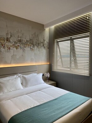 A modern bedroom with a large bed, a headboard with a textured wall art, a bedside table with a vase, and a window with blinds. - Fan's Hotel Ormoc (Ormoc)