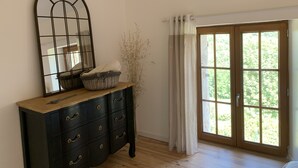 Une pièce avec une commode en bois foncé, un grand miroir et une fenêtre donnant sur un paysage verdoyant.
