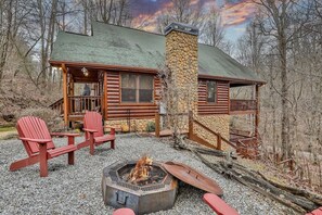 Una cabaña de troncos con chimenea de piedra, mobiliario exterior y un brasero.
