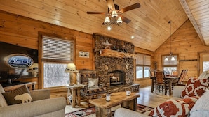 Ein Interieur einer Hütte mit Kamin aus Stein, Holzmöbeln, Deckenventilator und einem Schild für Blue Sky Cabin Rentals.