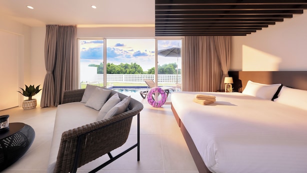 Een moderne hotelkamer met een groot bed, een rieten stoel, een klein tafeltje en uitzicht op het landschap.