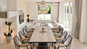 Een moderne eethoek met een lange tafel, meerdere stoelen en een wijnfles in het midden.