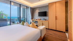 Ein modernes Hotelzimmer mit einem großen Bett, einem Schreibtisch, einem Fernseher und einem Balkon mit Meerblick.