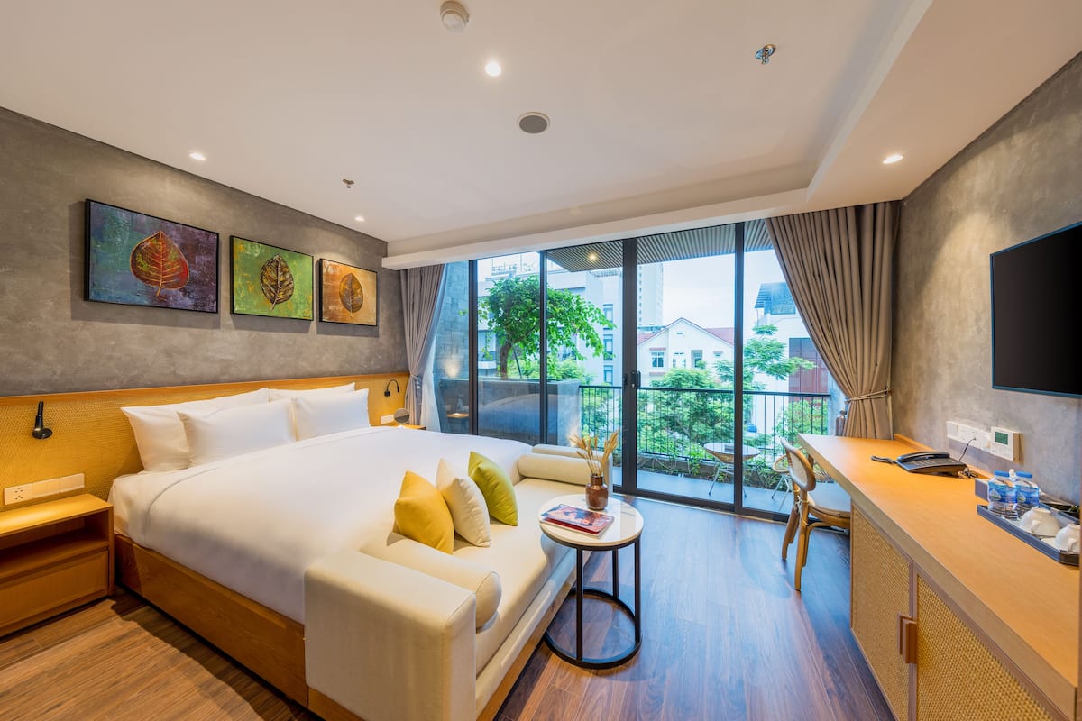 A modern hotel room with a large bed, a desk, and a balcony with a view of the city.