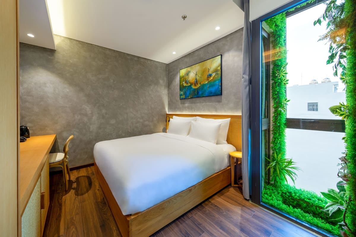 A modern bedroom with a large bed, a desk, and a window with a green wall.