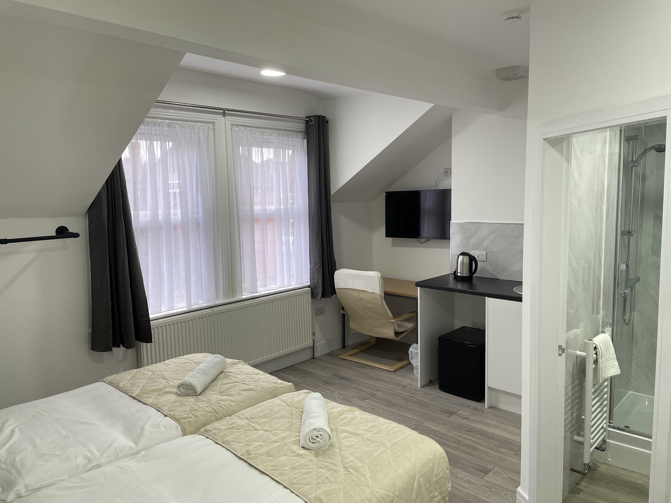 Habitación de hotel con dos camas, un escritorio, una silla, un televisor y zona de ducha.