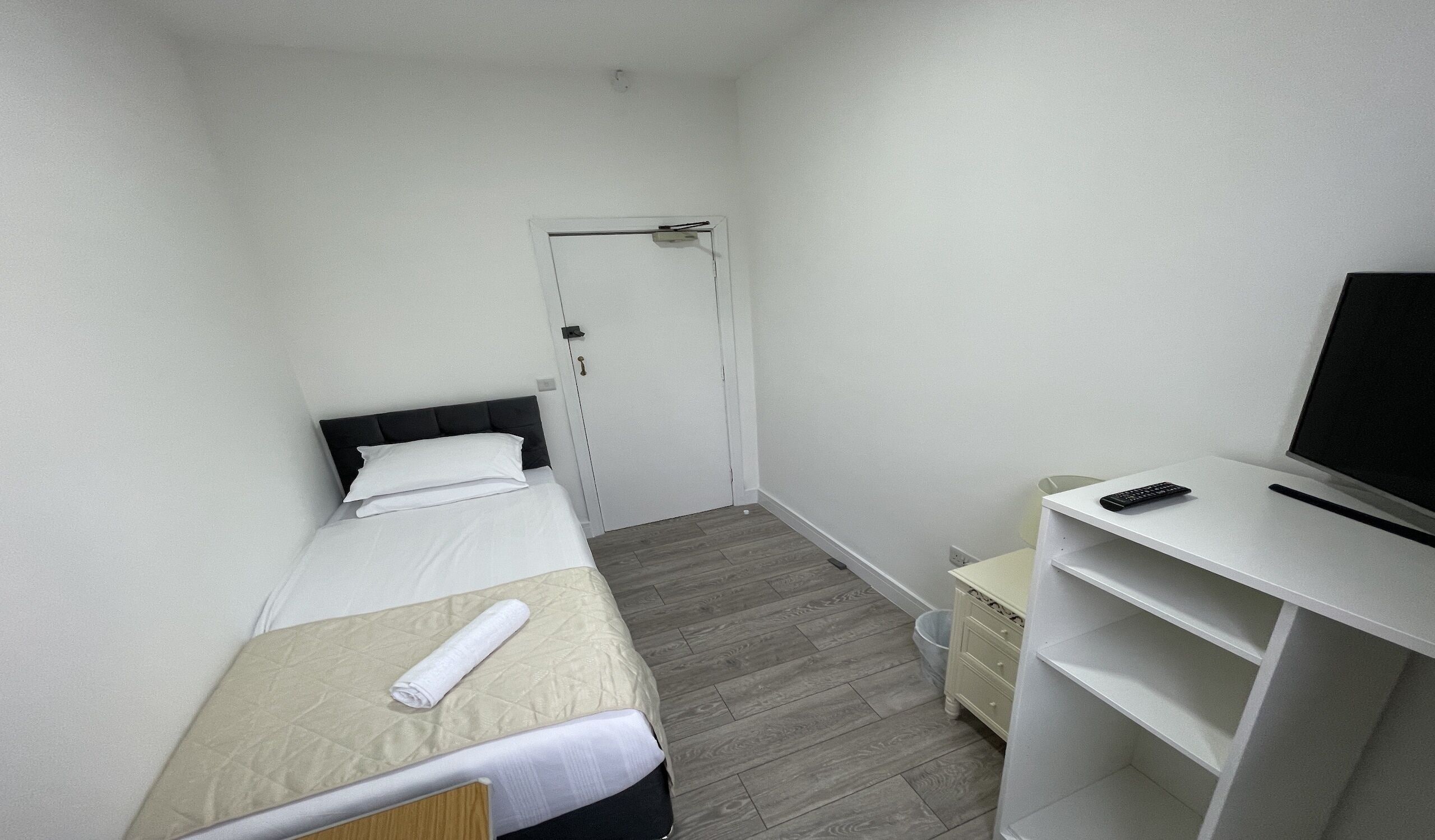 A small, neatly arranged hotel room with a single bed, a desk with a TV, and a chair.