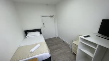 A small, neatly arranged hotel room with a single bed, a desk with a TV, and a chair.