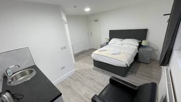 Una habitación de hotel moderna con cama, mesitas de noche, un pequeño escritorio, una silla y una zona de kitchenette.