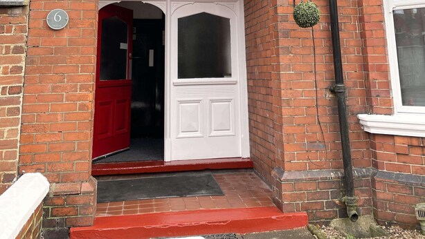 A red brick building with a white arched entrance, a red door, and a number '6' sign. - ISUITES (Newcastle-Under-Lyme)