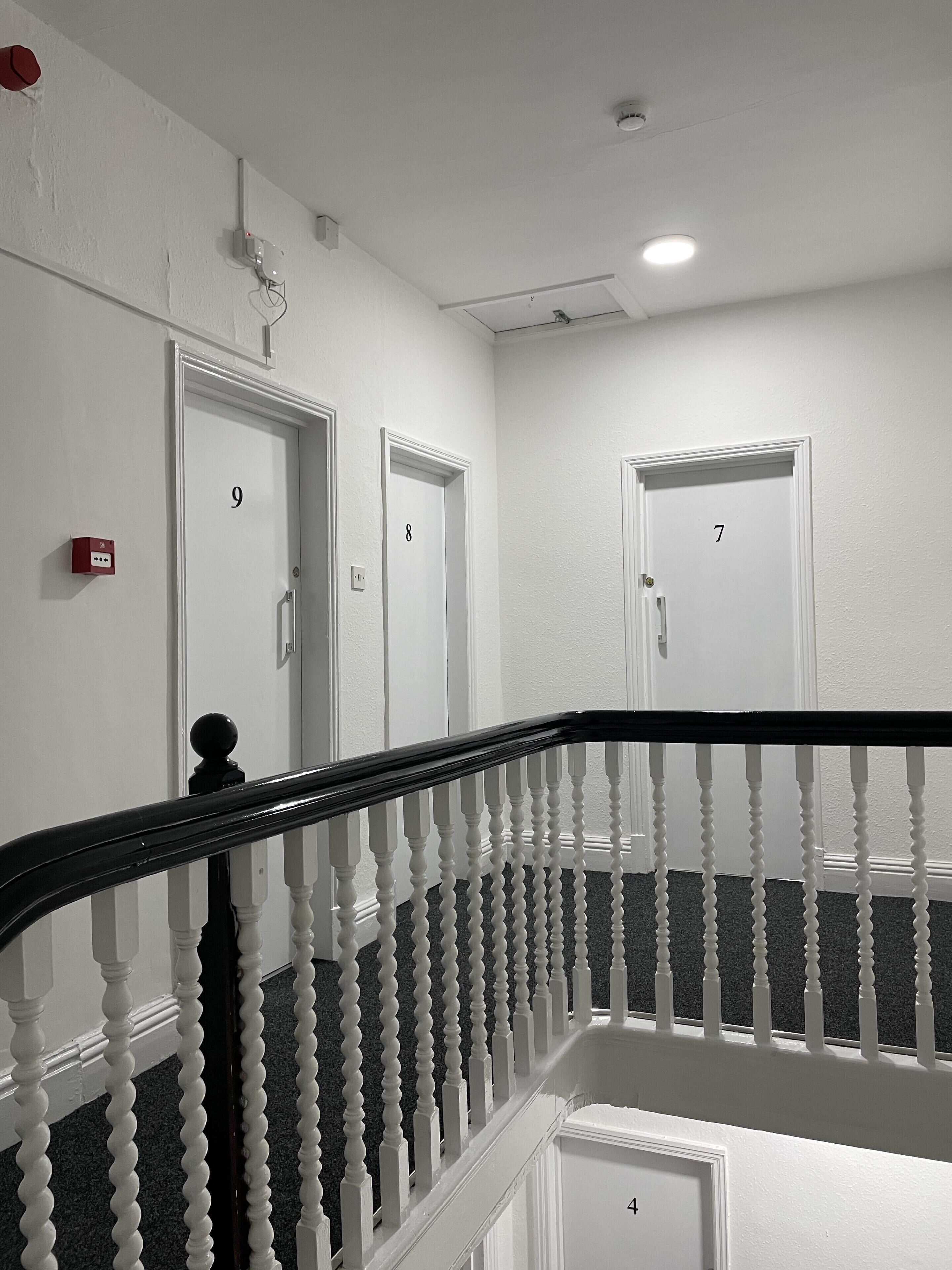 Interior com vários níveis, paredes brancas, portas numeradas e guarda-corpo preto e branco.