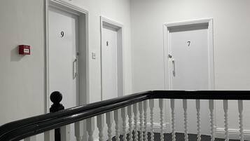 Interior com vários níveis, paredes brancas, portas numeradas e guarda-corpo preto e branco.