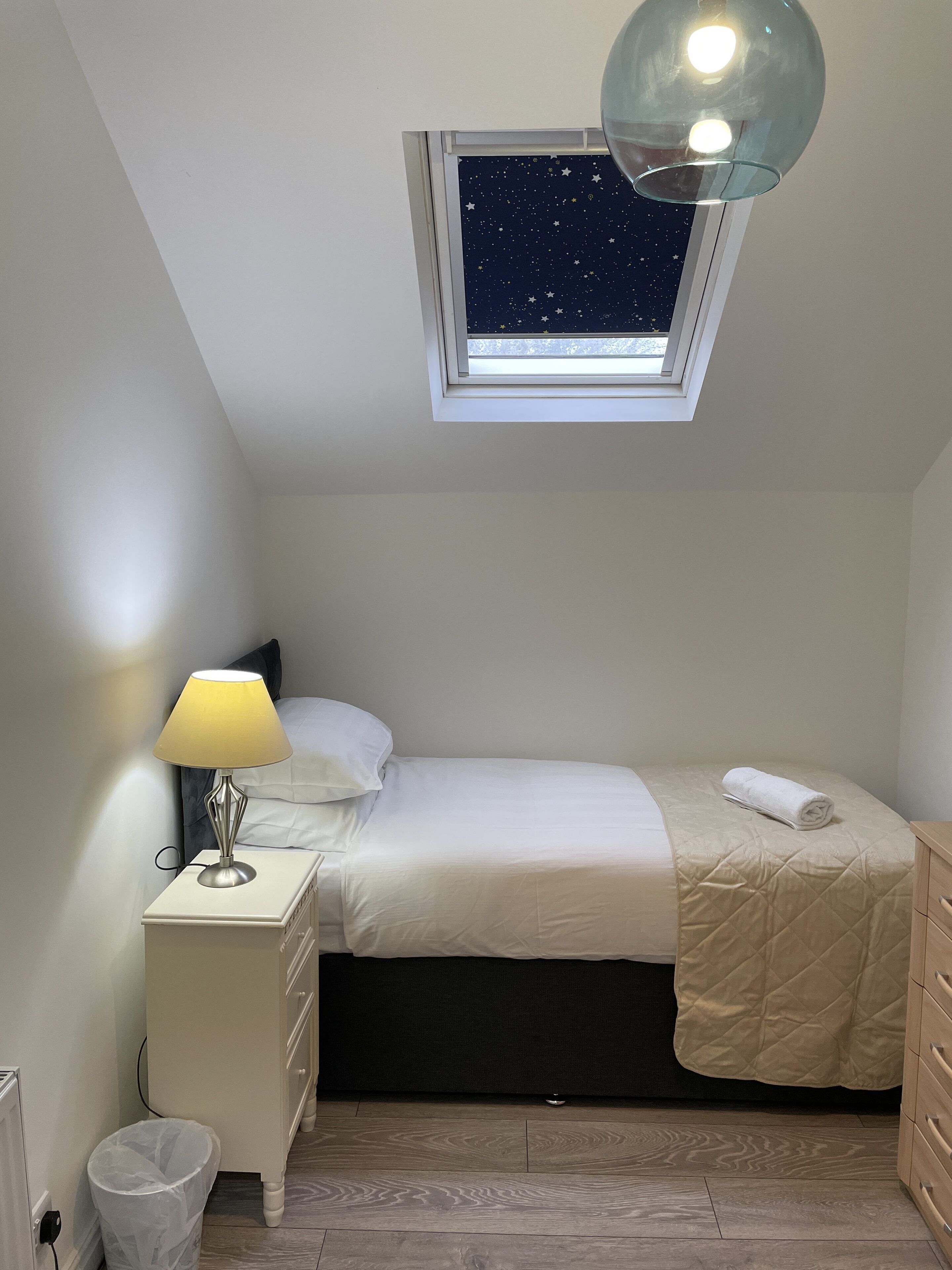 Een slaapkamer met dakraam, een bedlampje, een bed met quiltdeken en een nachtkastje.