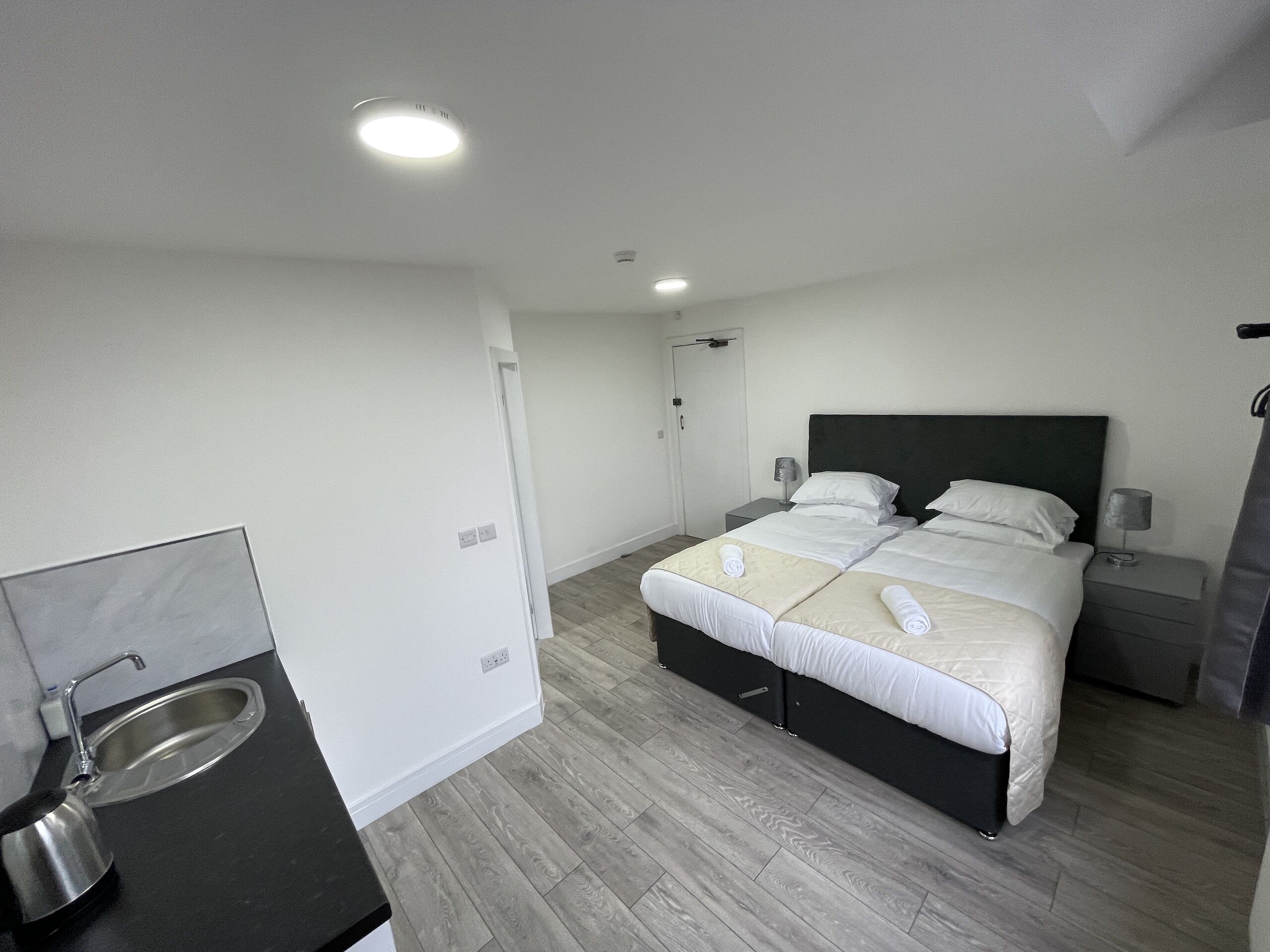 A hotel room with a bed, bedside tables, a small desk with a sink, and a mirror.