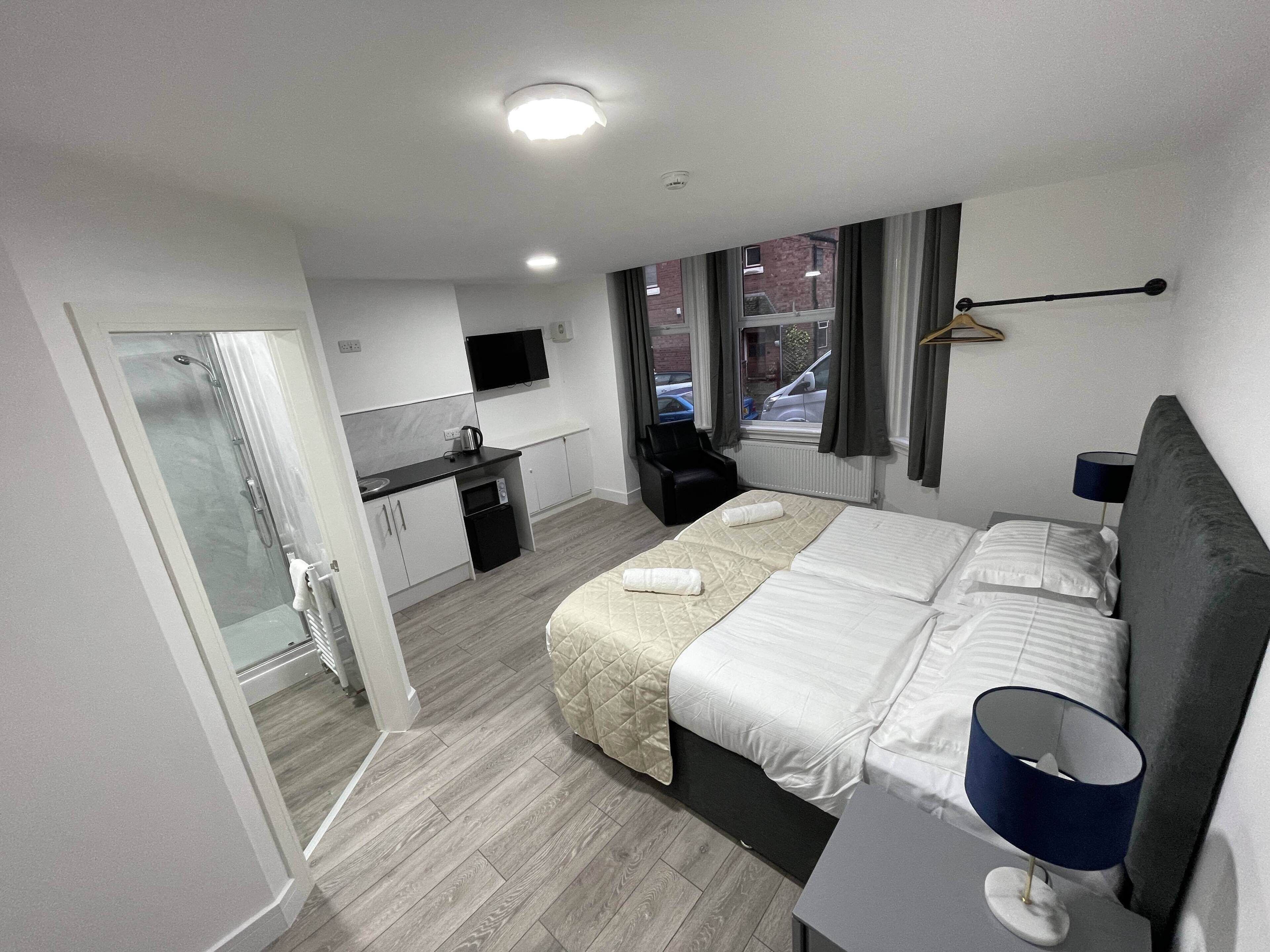 Una habitación de hotel moderna con cama, mesita de noche y una pequeña cocina.