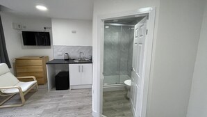 A compact hotel room with a kitchenette, a shower area, and a seating area with a chair. - ISUITES (Newcastle-Under-Lyme)