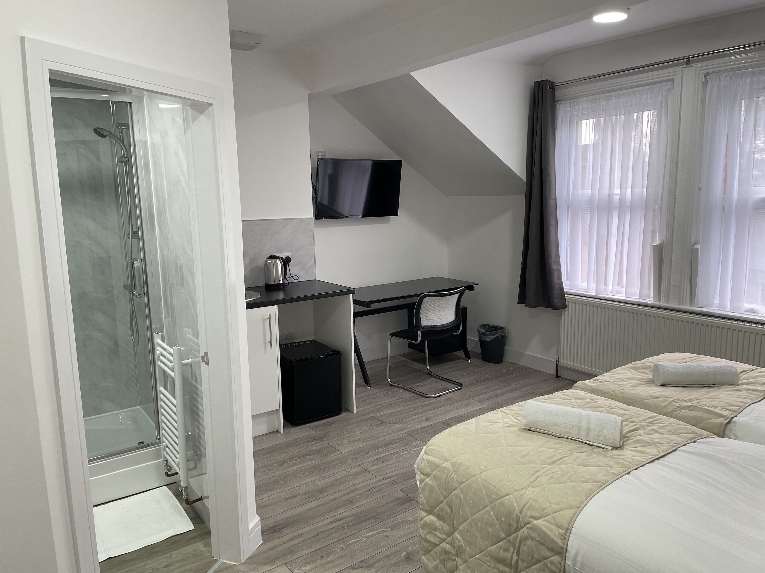Habitación de hotel compacta con cama, escritorio, silla, televisor y zona de ducha.
