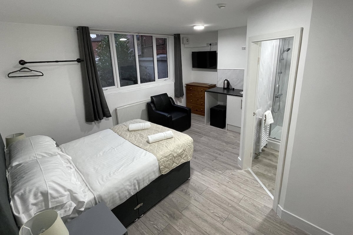 A modern hotel room with a bed, a desk, a chair, and a shower area.