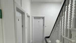 A narrow, carpeted hallway with white walls and doors numbered 4 and 6. A staircase with white balusters and a black handrail leads to an upper floor. - ISUITES (Newcastle-Under-Lyme)