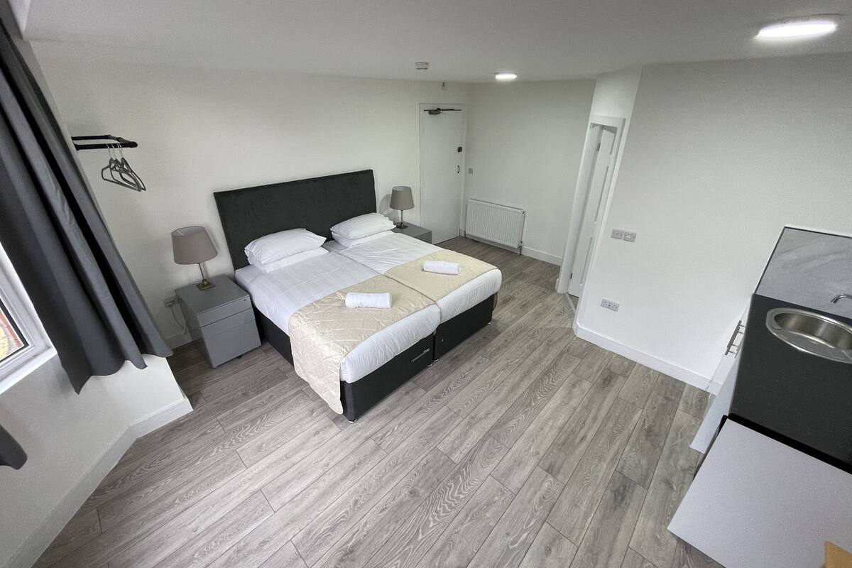 A modern hotel room with a large bed, bedside tables, a desk, and a kitchenette.