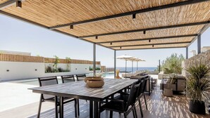 Une terrasse extérieure avec une table et des chaises en bois, une piscine et une vue sur la mer.