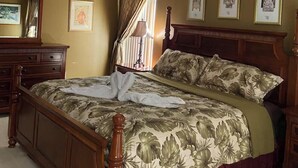Une chambre à coucher avec un lit, un ventilateur de plafond, une commode et des tableaux encadrés accrochés au mur.