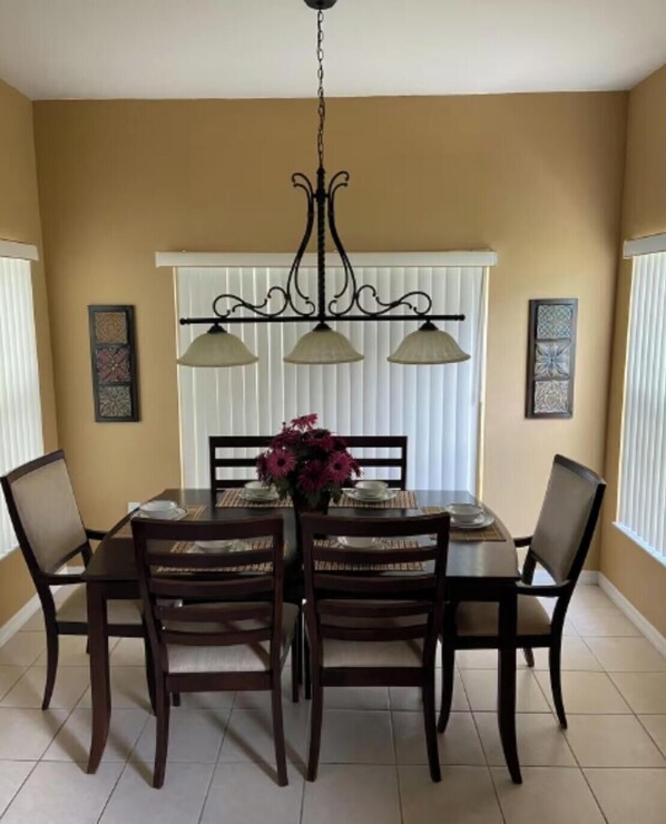 A dining room with a table set for four, surrounded by chairs, a chandelier, and two wall-mounted lamps.